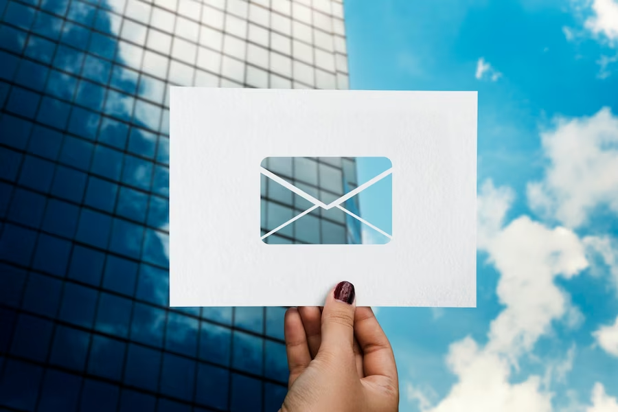 Hand holding paper with envelope cut-out, building and sky in background