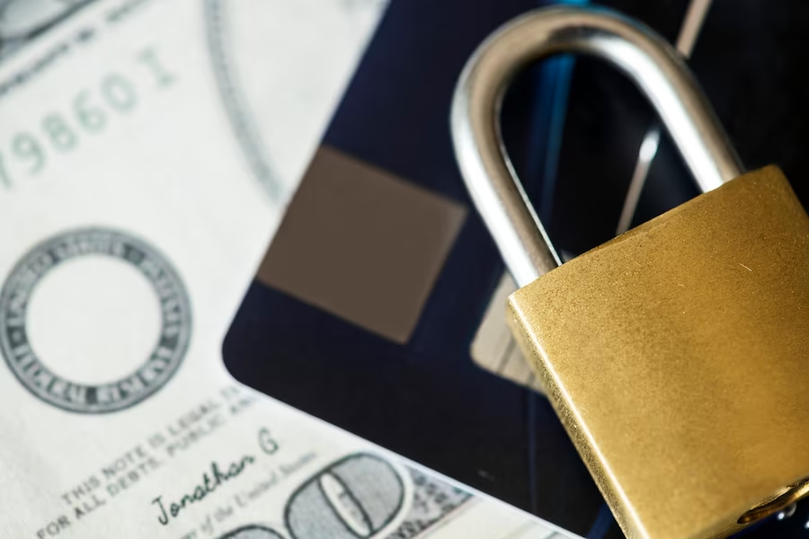 Close-up of dollar bill, ATM card, and padlock grouped together