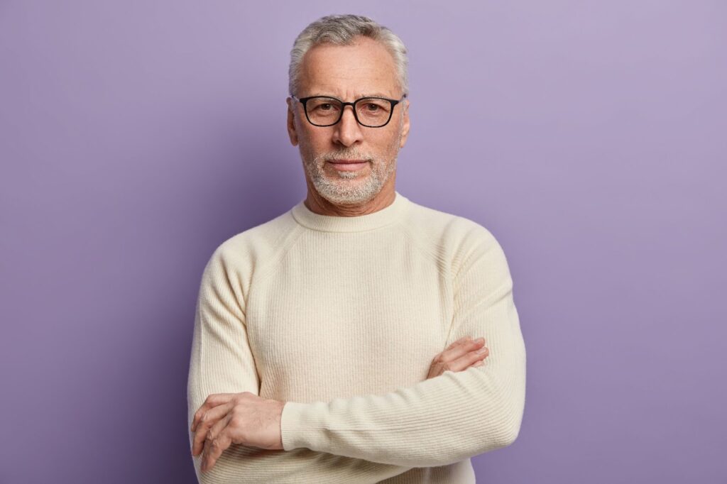 a senior man in a white sweater and eyeglasses looking at the camera